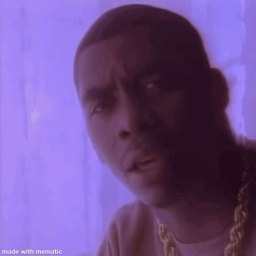 A man in purple lighting gives a serious look toward the camera.
