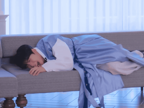 a man in a blue robe is laying on a couch with his eyes closed