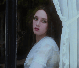a woman in a white shirt looks out a window