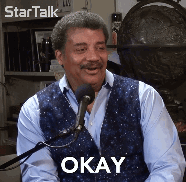 a man sitting in front of a microphone with okay written on his chest