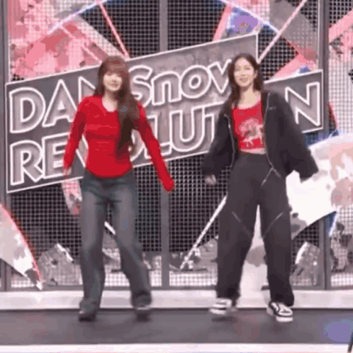 two women are dancing on a stage in front of a sign that says `` dan snow revolution '' .