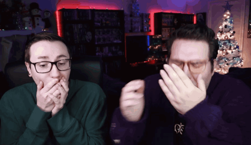 two men are covering their mouths with their hands in front of a christmas tree