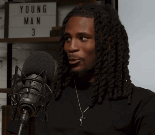a man with dreadlocks is speaking into a microphone in front of a young man 3 sign