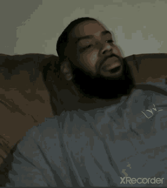 a man with a beard is laying on a couch wearing a grey shirt that says lw