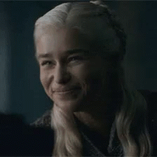 Daenerys Targaryen gives a small, shy smile in dim light.
