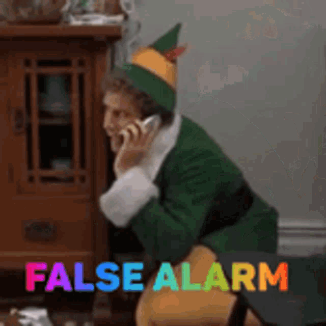 a man dressed as an elf is talking on a cell phone with the words false alarm above him .