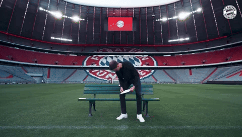 a man sits on a bench in an empty soccer stadium with the bayern munchen logo on the wall