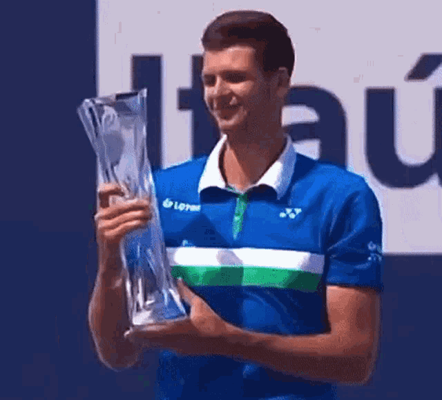 a man in a blue shirt is holding a trophy and smiling