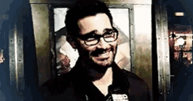 a man wearing glasses and a beard is smiling in front of a door .
