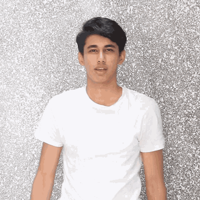 a young man in a white t-shirt is standing in front of a silver background