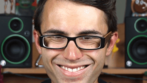 a man wearing glasses makes a funny face in front of green speakers