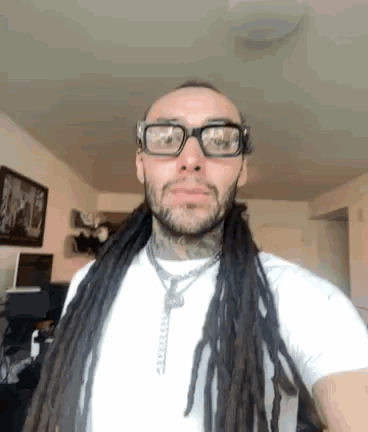 a man with dreadlocks and glasses is wearing a white shirt .
