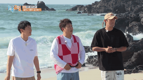 three men are standing on a beach with a sign that says 1 2 on it