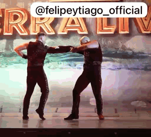 two men are dancing on a stage in front of a sign that says ferra live