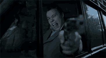 a man is pointing a gun out of a car window at someone .