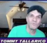 tommy tallarico is wearing a green shirt and a baseball cap while looking at the camera .