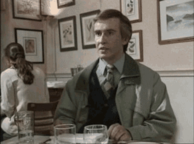 A man in a coat sits at a restaurant table looking resigned.