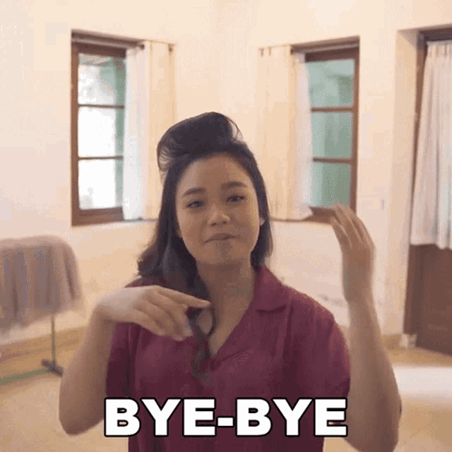 a woman in a pink shirt says bye-bye in front of a window