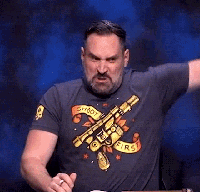 a man with a beard wearing a t-shirt with a scorpion on it scratches his head