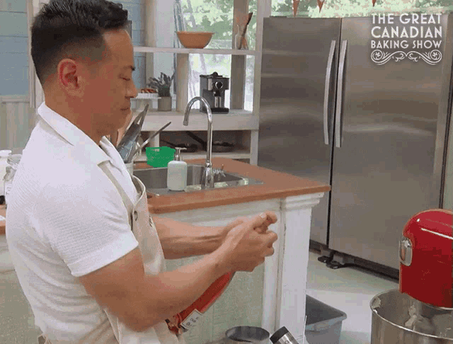 a man in a kitchen with the great canadian baking show in the background