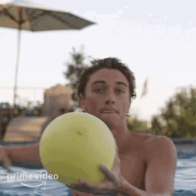 a shirtless man is in a pool holding a yellow ball .