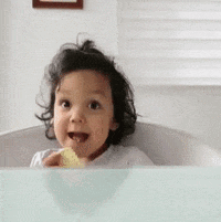 A smiling toddler in a bathtub looks excitedly toward the camera.