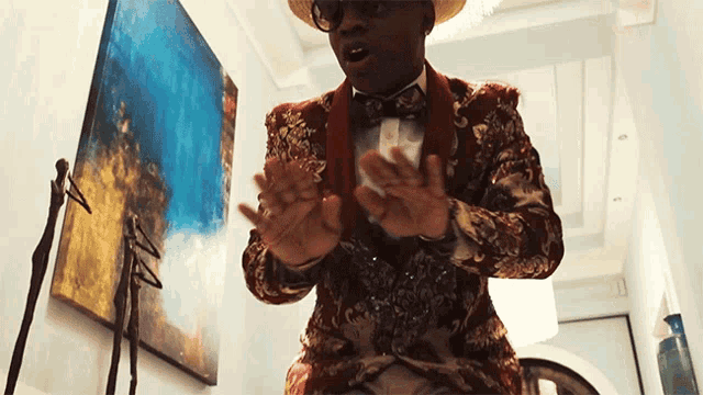 a man in a suit and bow tie is clapping his hands in front of a painting