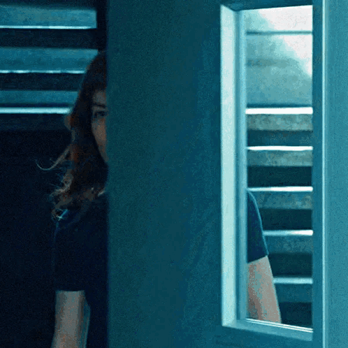 a woman in a black shirt is peeking out from behind a blue door