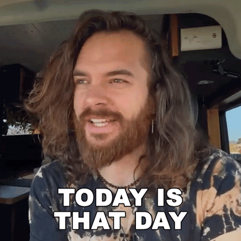 a man with long hair and a beard is sitting in a car and says today is that day