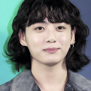 A close-up of Jungkook with dark wavy hair looks calmly toward the camera against a mint background.