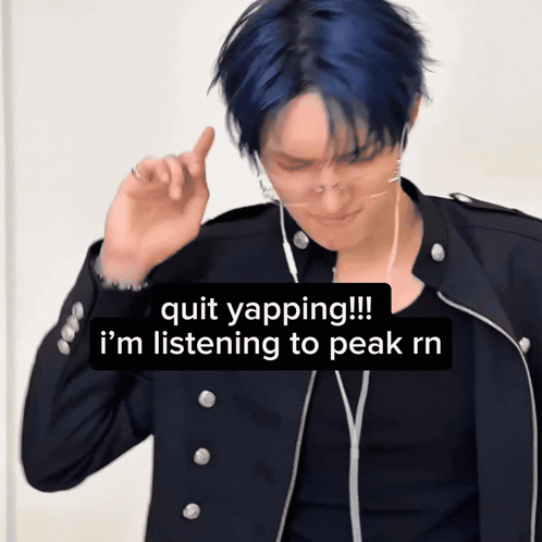 a man with blue hair is wearing ear buds and a black jacket and says quit yapping !!!