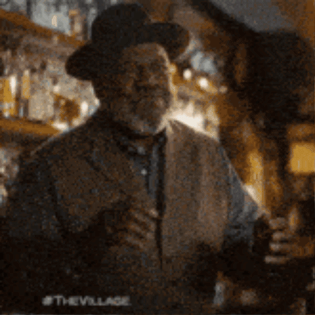 a man in a cowboy hat is standing in a bar holding a glass of beer