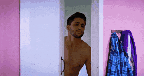 a shirtless man stands in a doorway with a blue plaid shirt hanging on a rack