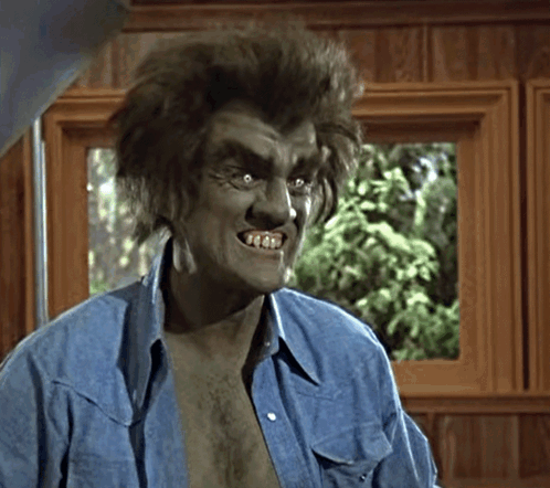 A snarling green monster in a blue shirt bares sharp teeth indoors.