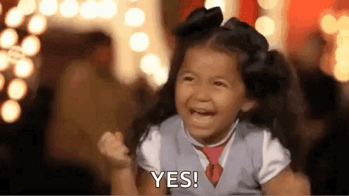 A smiling child raises a fist and says “YES!” on a stage-like set.