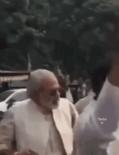 An older man in white clothing dances outdoors among people.