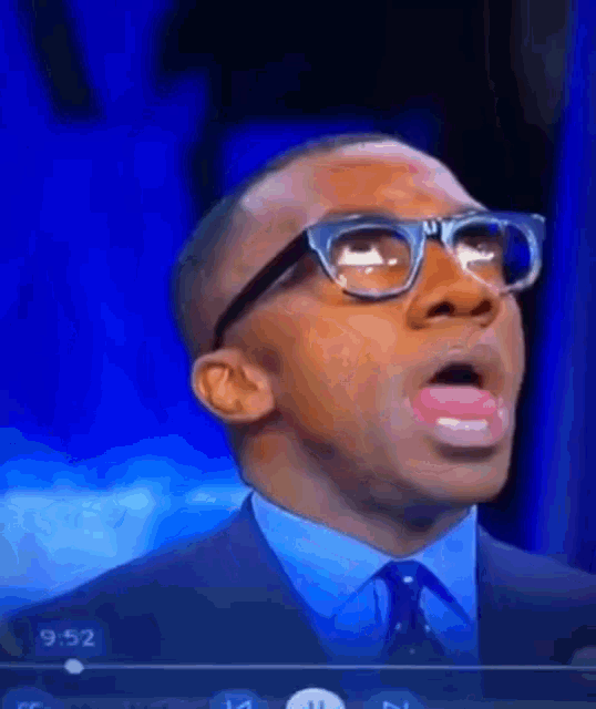 a man wearing glasses and a blue shirt is making a funny face with his mouth open