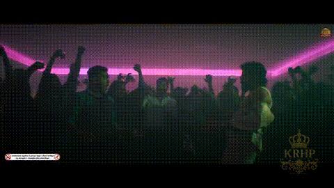 a crowd of people are dancing in a dark room with pink lights .