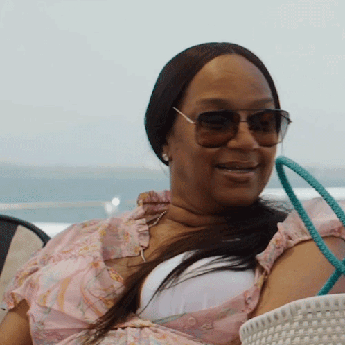 a woman wearing sunglasses and a pink top smiles