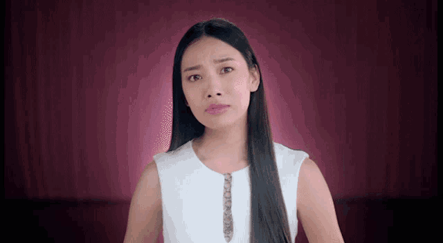 a woman with long hair and a white top is making a funny face