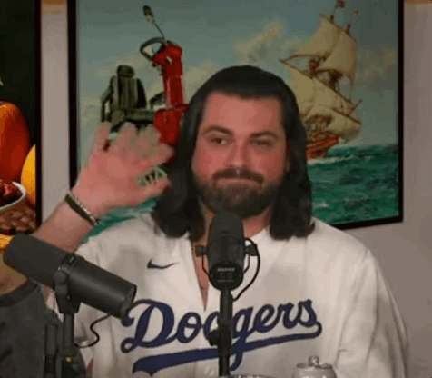 a man with long hair and a beard is wearing a dodgers jersey and waving at the camera .
