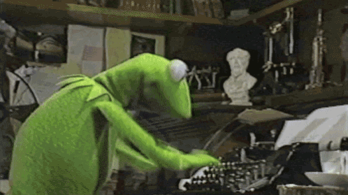 Kermit furiously types at a cluttered keyboard workstation.