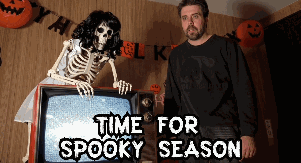 a man is standing next to a skeleton in front of a tv that says time for spooky season