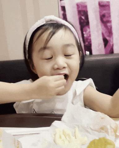 A young child happily eats food at a table.