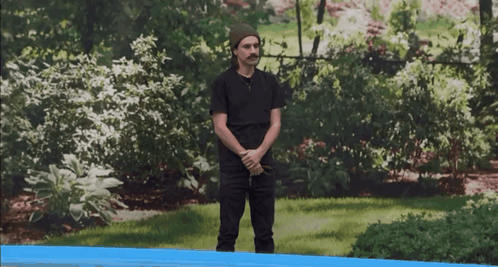 a man in a black shirt and a beanie stands in a garden
