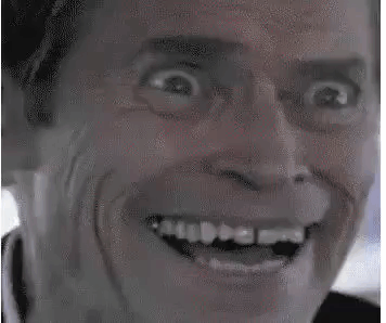 A man grins intensely in a grainy close-up.