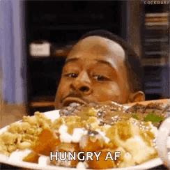 A man stares intensely at a piled plate of food with “HUNGRY AF.”