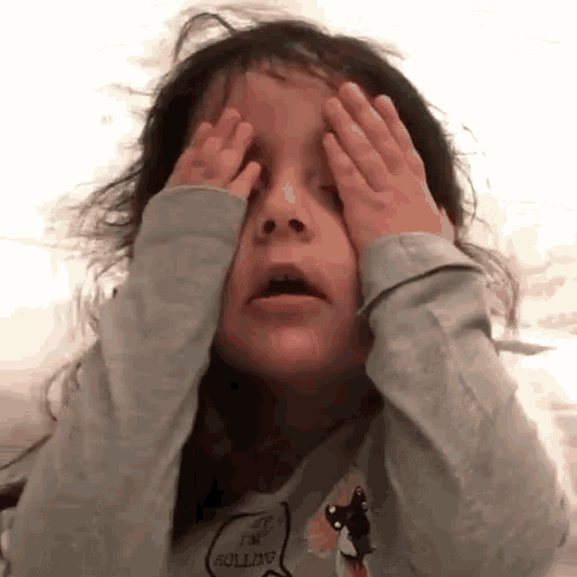 A young girl covers her face with both hands in exasperation.