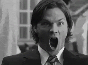 a black and white photo of a man in a suit and tie making a surprised face .