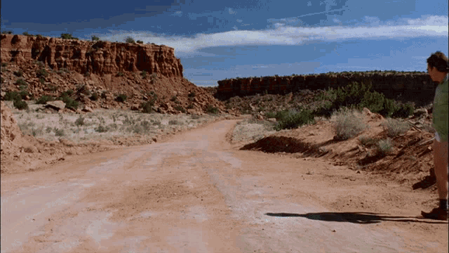 a man is standing on a dirt road in the desert